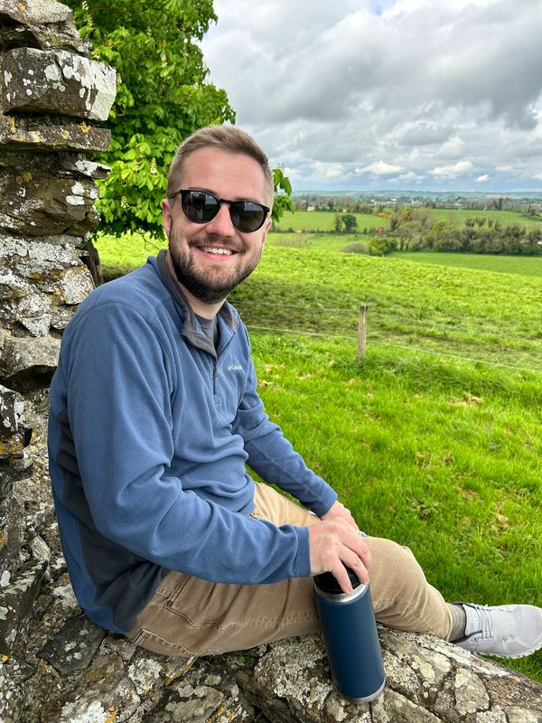 Man in sunglasses sitting on rocks with a green field behind him.