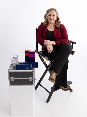 The Owner, Teresa Lain,  in a red jacket, sits on a director's chair next to beauty product boxes.