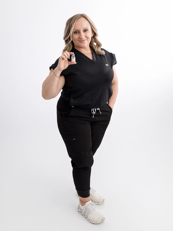 Woman in black scrubs holding a vaccine vial, smiling confidently.