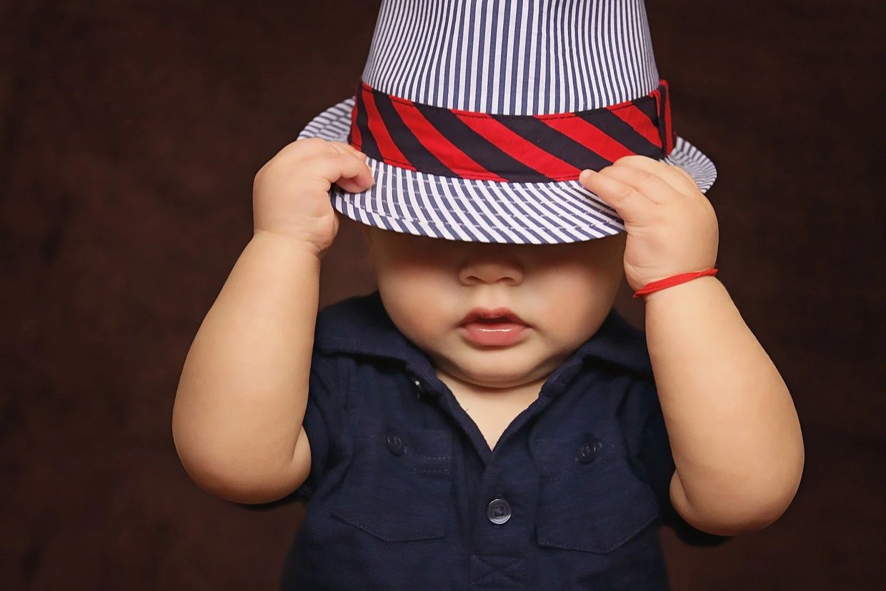 Toddler boy with blue shirt holding hat with red and blue striped band.