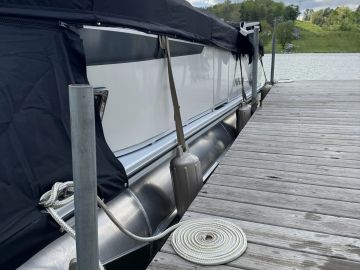 A pontoon boat docked beside a wooden pier with coiled rope.