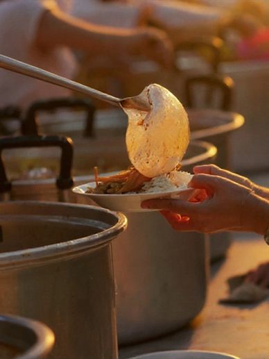Serving hot food from large pots at a communal meal.