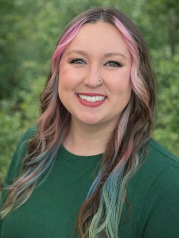 Smiling woman with colorful hair and green top outdoors.