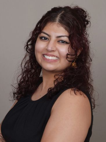 Smiling woman with curly hair in a black sleeveless top against a neutral background.