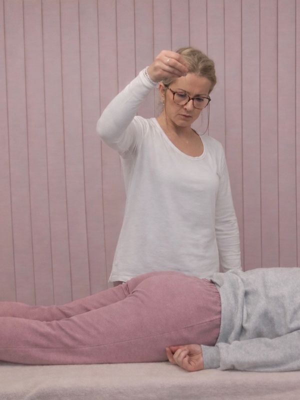 A woman performing a pendulum healing technique on a person lying down.