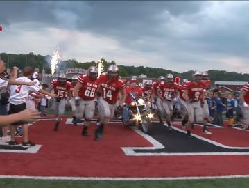 High school football team running onto the field with a motorcycle leading.