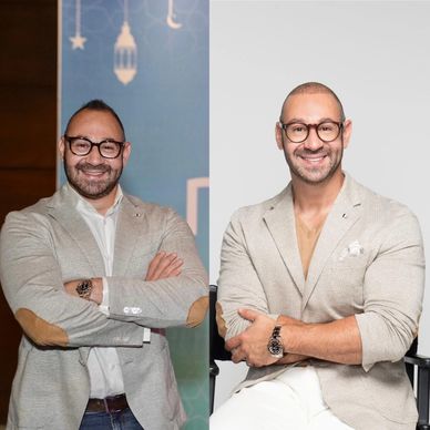 Two men in glasses and beige blazers smiling.