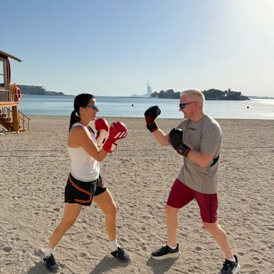 Two people boxing on a beach at sunrise or sunset.