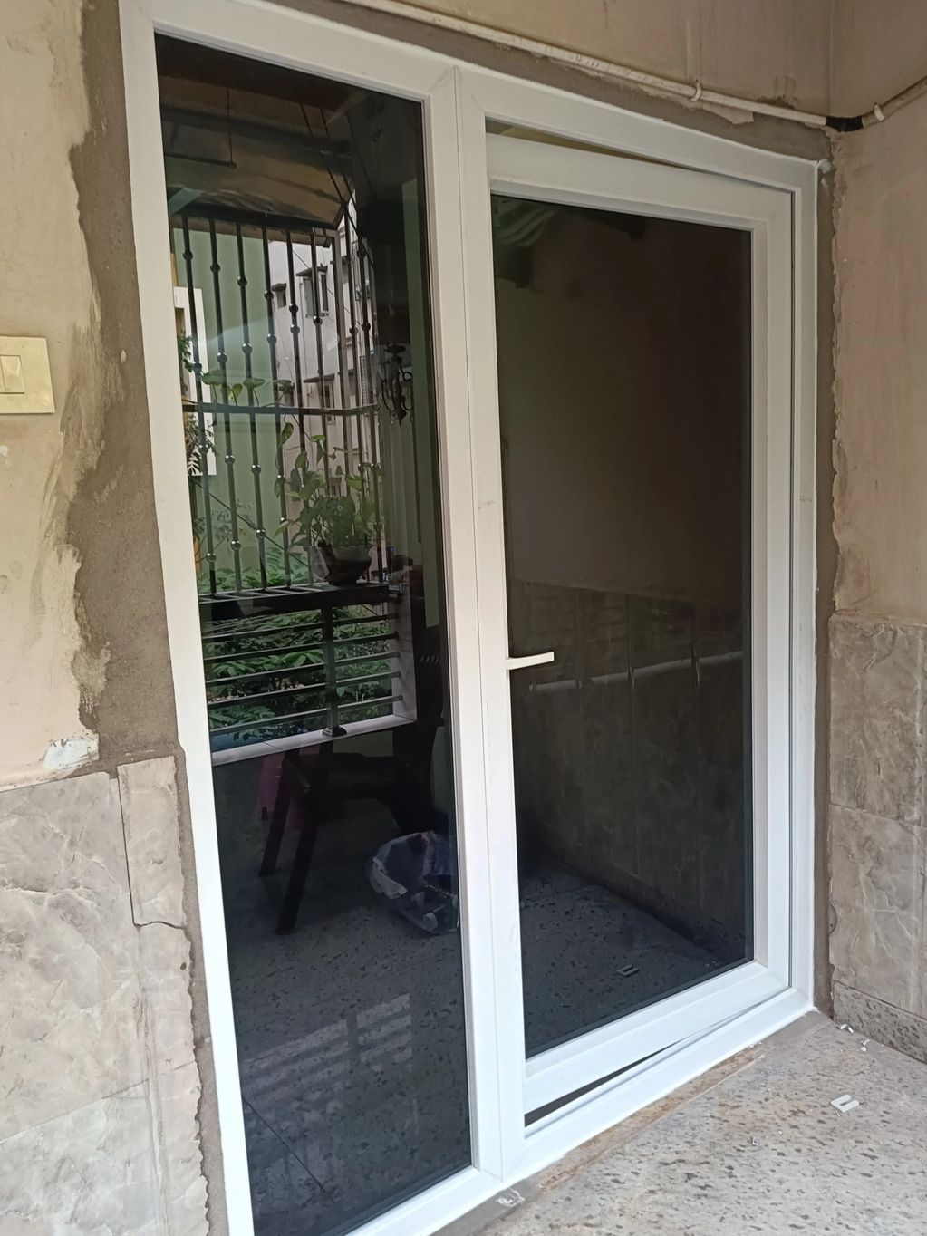 White framed sliding glass door with reflections and plants outside.