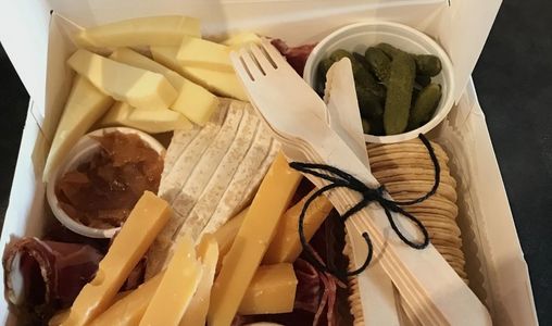 Gourmet charcuterie box with cheese, crackers, pickles, and wooden utensils.