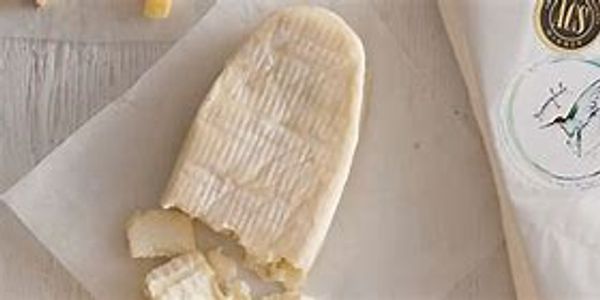A piece of soft cheese partially cut on parchment paper beside cheese packaging.