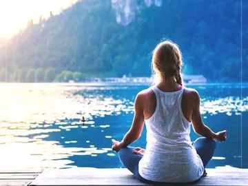 Woman meditating by a serene lake at sunrise.
