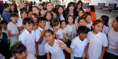 Group of smiling schoolchildren with adults in an indoor setting.