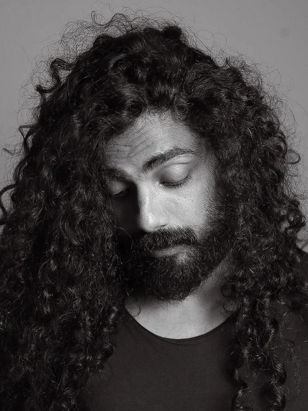 Black and white portrait of a man with long curly hair and a beard looking down.