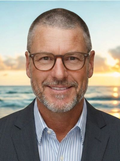 Michael Zapkowski. Smiling man in glasses and suit with ocean sunset background.