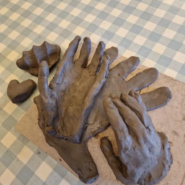 Clay sculptures of hands and a heart on a checkered surface.