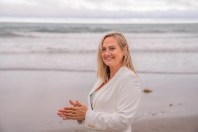 Smiling woman in white jacket on the beach.