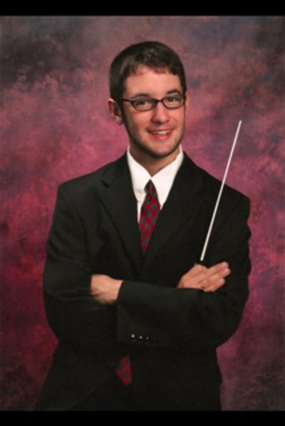 Young man in suit holding a conductor's baton against a textured background.