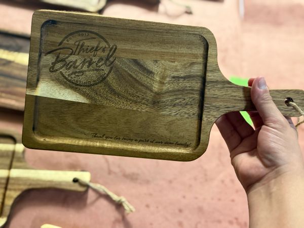 Hand holding a wooden serving board with a logo and message engraved.