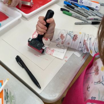 Child using a brayer to apply ink or paint on a surface during an art activity.