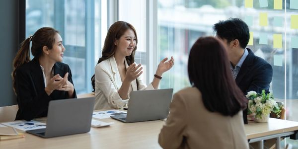 Four colleagues engaged in a lively discussion around a table with laptops.