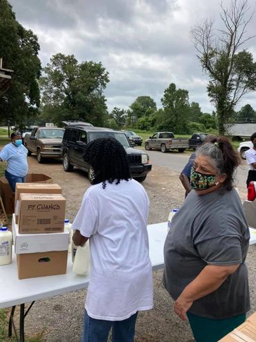 People wearing masks distributing supplies outdoors on a cloudy day.