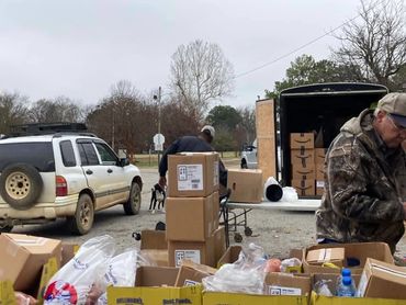 Volunteers unloading and organizing boxes and supplies outdoors on a cloudy day.