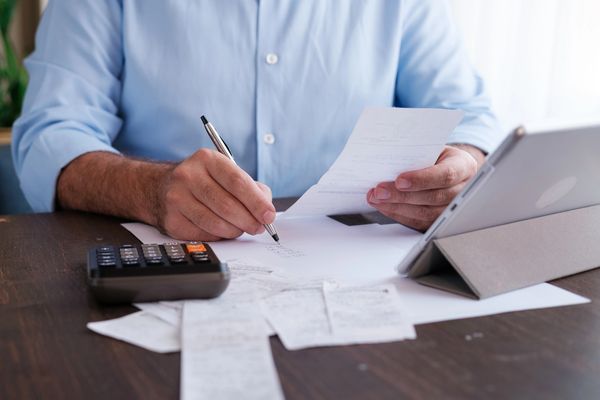 A man writing a notes on paper in front of Tablet With calculator