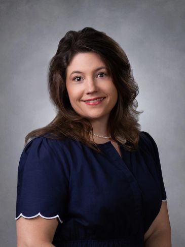Smiling woman in a navy blue dress with pearl necklace.