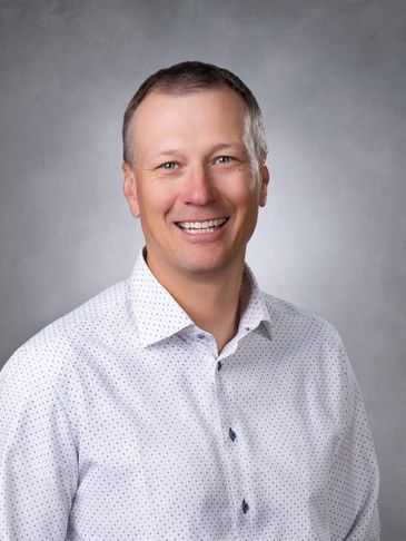 Smiling man in a white dotted shirt against a gray background.