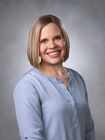 Smiling woman with blonde bob haircut wearing a light blue blouse.