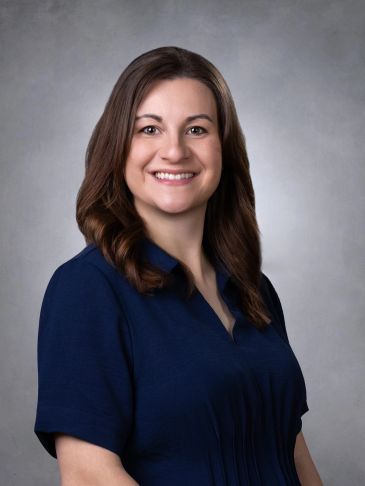 Smiling woman with brown hair in a navy blue top against a gray background.