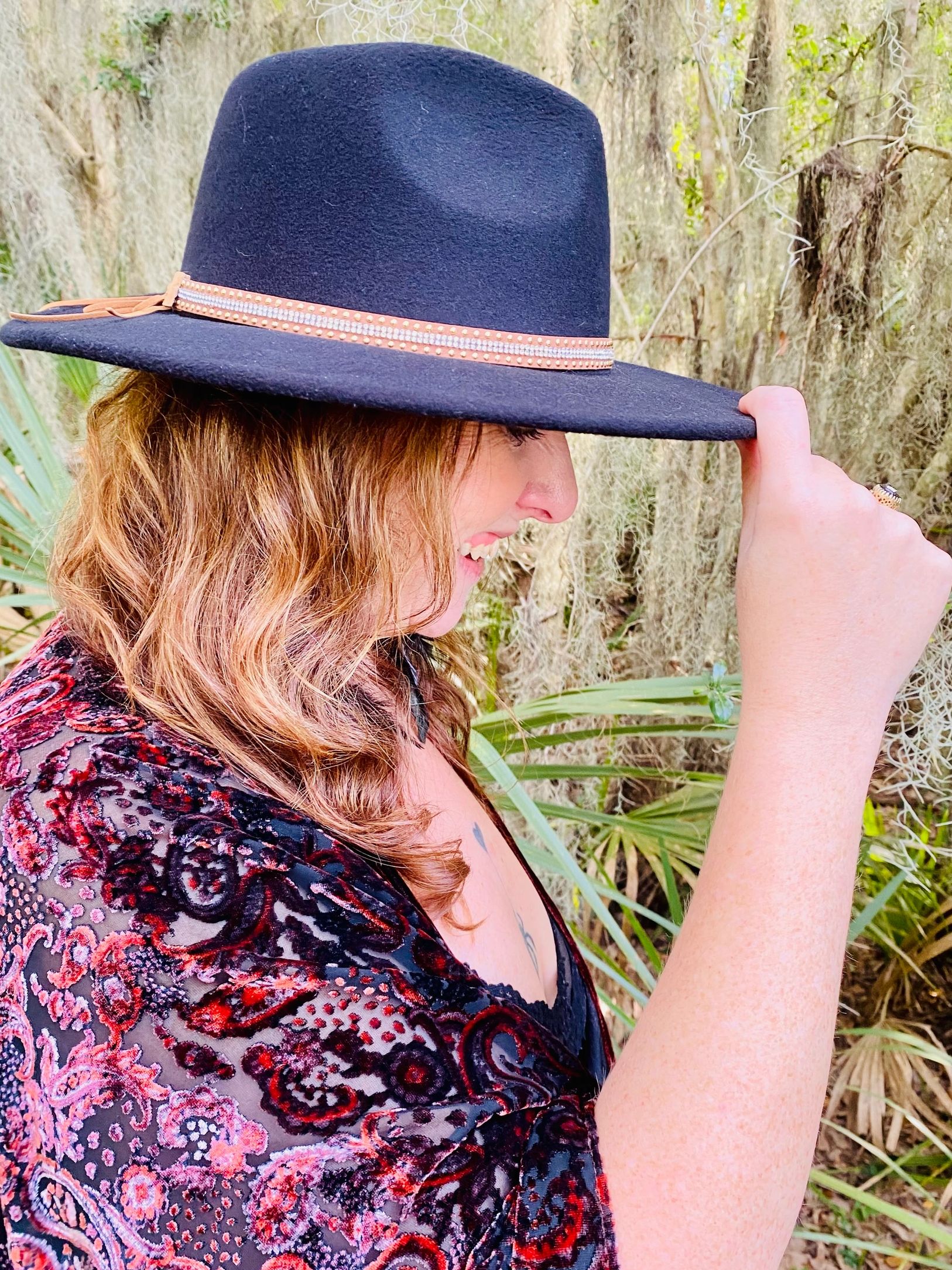 Woman smiling while adjusting a black hat outdoors.