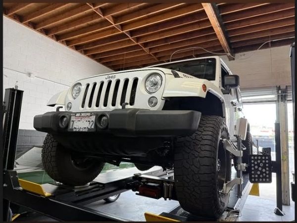 White Jeep Wrangler on a lift in a garage for maintenance.