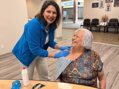 Caregiver assisting elderly woman with therapy, both smiling.