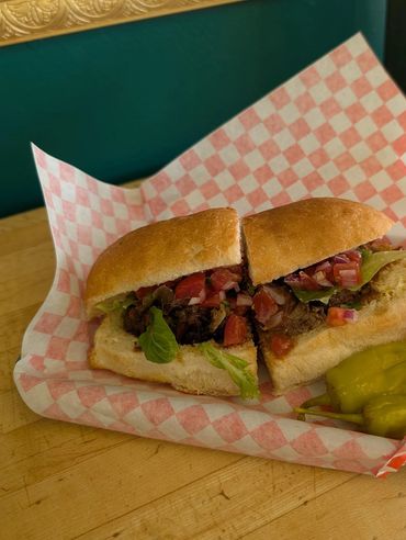 A sandwich with lettuce, tomatoes, and meat on a checkered paper.