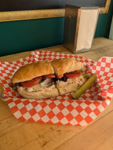 A sandwich with lettuce, tomato, and a pickle on a checkered paper.