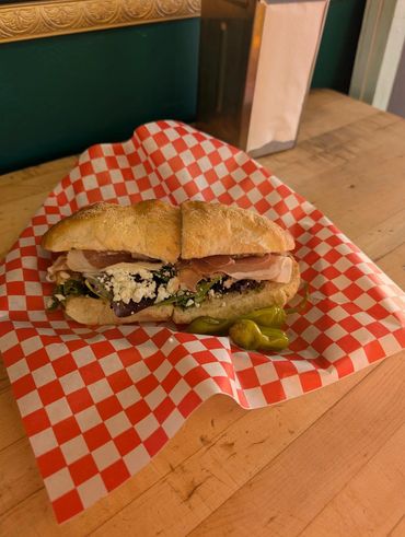 A sandwich with ham, cheese, and greens on checkered paper.