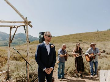 Groom waiting at an outdoor wedding ceremony with musicians in the background.