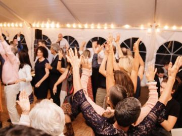 A lively group dancing with raised hands under string lights.
