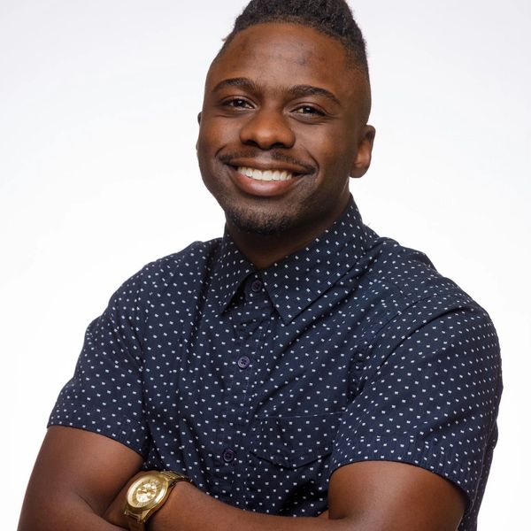 Confident man smiling with arms crossed, wearing a patterned navy shirt and gold watch.
