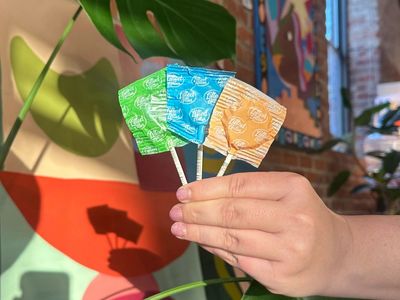 Hand holding three colorful lollipops against a vibrant background.