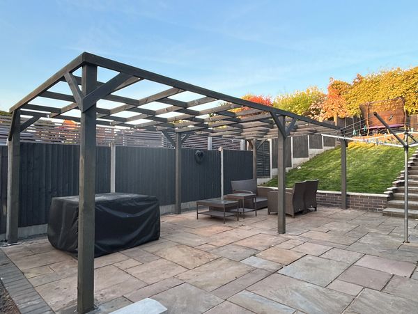 Backyard patio with pergola, seating, and stairs leading to a grassy area.