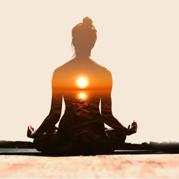 Silhouette of a person meditating with a sunset over the ocean within their form.