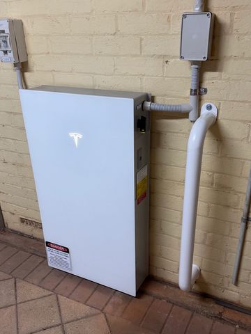 Tesla Powerwall mounted on an exterior wall with electrical conduit and junction box.