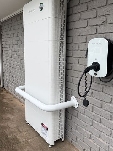 Outdoor white heat pump mounted on a brick wall with a security camera nearby.