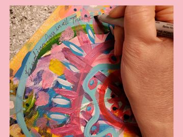 Hand writing words on a colorful painting.  The words say "Finding Joy in all things"