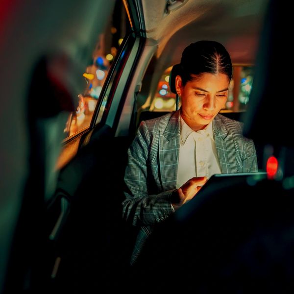 A woman in a blazer using a tablet inside a car at night.
