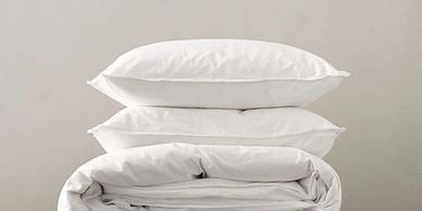 Stack of three white pillows on top of a folded white duvet.