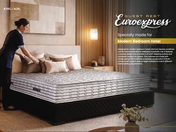 A hotel staff arranges pillows on a neatly made bed with a Euroexpress mattress.